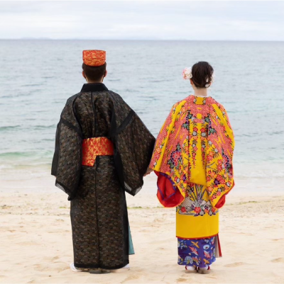 沖縄の伝統衣装を着て海を眺めて立っている夫婦の後ろ姿